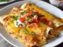 A baking dish filled with golden chicken enchiladas smothered in creamy queso sauce, topped with melted cheese and fresh cilantro.