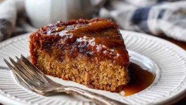 Moist Amish applesauce cake topped with glaze and sprinkled with cinnamon on a rustic serving plate.