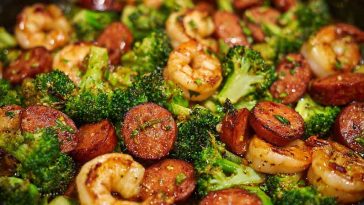 Honey garlic shrimp with savory sausages and roasted broccoli served in a skillet, glazed with golden sauce.