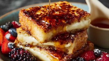 Golden slices of crème brûlée French toast with caramelized tops and powdered sugar on a serving plate.