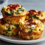Savory egg muffins filled with spinach, feta cheese, and sun-dried tomatoes, baked golden in a muffin tin.
