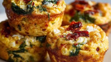 Savory egg muffins filled with spinach, feta cheese, and sun-dried tomatoes, baked golden in a muffin tin.