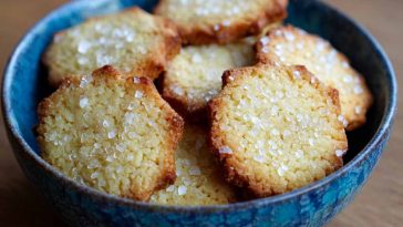 Alt Text: Golden French salted butter cookies stacked on a rustic wooden board with sea salt flakes
