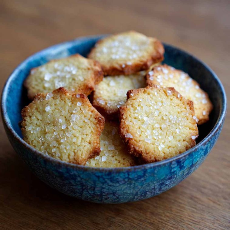 Alt Text: Golden French salted butter cookies stacked on a rustic wooden board with sea salt flakes