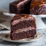 A decadent slice of Ina Garten’s chocolate fudge cake with glossy ganache frosting and chocolate shavings.