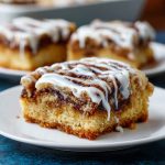 Golden cinnamon roll bliss bars drizzled with icing, layered with cinnamon sugar swirls, and served on a dessert tray.