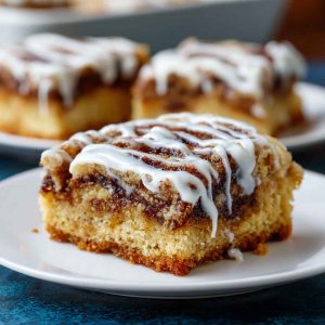 Golden cinnamon roll bliss bars drizzled with icing, layered with cinnamon sugar swirls, and served on a dessert tray.