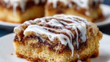 Golden cinnamon roll bliss bars drizzled with icing, layered with cinnamon sugar swirls, and served on a dessert tray.