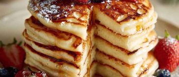 Stack of golden fluffy pancakes topped with butter and maple syrup, served on a breakfast table.