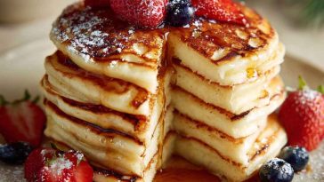Stack of golden fluffy pancakes topped with butter and maple syrup, served on a breakfast table.
