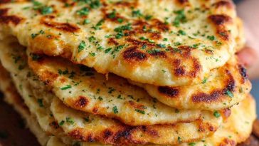 Golden keto naan bread brushed with garlic butter, served with curry and fresh herbs on a rustic plate.
