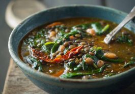 Bowl of spinach, lentil, and butter bean soup garnished with fresh herbs