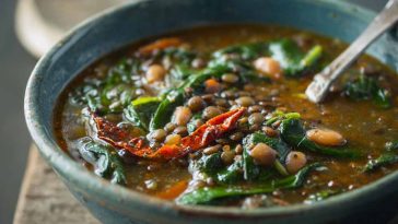 Bowl of spinach, lentil, and butter bean soup garnished with fresh herbs