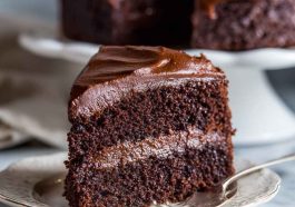 A decadent slice of Ina Garten’s chocolate fudge cake with glossy ganache frosting and chocolate shavings.
