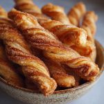 Golden-brown cinnamon twists with flaky layers, dusted with sugar and cinnamon, served on a rustic tray with coffee.