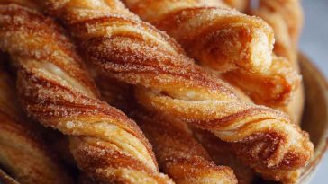 Golden-brown cinnamon twists with flaky layers, dusted with sugar and cinnamon, served on a rustic tray with coffee.