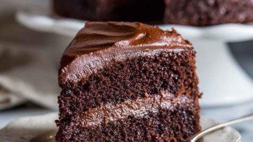 A decadent slice of Ina Garten’s chocolate fudge cake with glossy ganache frosting and chocolate shavings.
