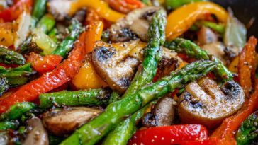 A skillet filled with colorful sautéed vegetables including bell peppers, zucchini, carrots, and broccoli, garnished with fresh herbs.