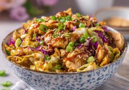 A bowl filled with sautéed ground chicken, shredded cabbage, carrots, and green onions, drizzled with soy sauce and sesame seeds.