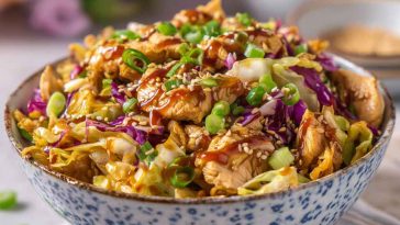 A bowl filled with sautéed ground chicken, shredded cabbage, carrots, and green onions, drizzled with soy sauce and sesame seeds.