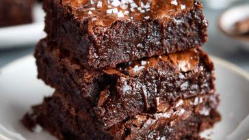 A stack of fudgy zero sugar brownies made with Greek yogurt, topped with a dusting of cocoa powder and fresh raspberries.