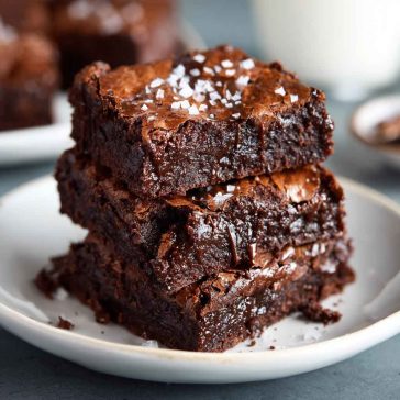A stack of fudgy zero sugar brownies made with Greek yogurt, topped with a dusting of cocoa powder and fresh raspberries.