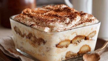 Coquito tiramisu layered with mascarpone cream and dusted with cinnamon in a glass dish.