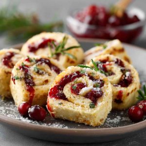 Festive Christmas cranberry roll ups filled with cream cheese, cranberries, and herbs, sliced into bite-sized pinwheels on a holiday platter.