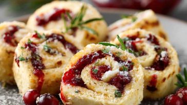 Festive Christmas cranberry roll ups filled with cream cheese, cranberries, and herbs, sliced into bite-sized pinwheels on a holiday platter.