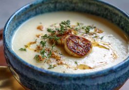 Creamy roasted garlic soup served in a rustic bowl, garnished with fresh herbs and crusty bread on the side.