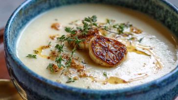 Creamy roasted garlic soup served in a rustic bowl, garnished with fresh herbs and crusty bread on the side.