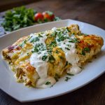 A baking dish filled with golden chicken enchiladas smothered in sour cream white sauce, topped with melted cheese and fresh cilantro.