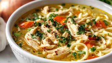 Bowl of classic ginger garlic chicken noodle soup with fresh herbs and noodles