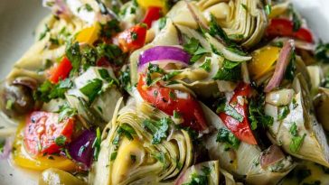 A vibrant bowl of artichoke salad with marinated artichoke hearts, cherry tomatoes, olives, red onion, and fresh herbs.