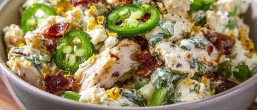A bowl of jalapeno popper chicken salad with shredded chicken, diced jalapeños, crispy bacon, and melted cheese, garnished with fresh herbs.