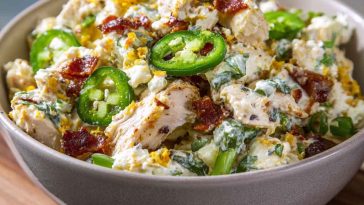 A bowl of jalapeno popper chicken salad with shredded chicken, diced jalapeños, crispy bacon, and melted cheese, garnished with fresh herbs.