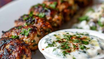 Golden chicken kofta skewers served with creamy garlic yogurt sauce and fresh herbs on a rustic plate.