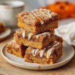 Delicious pumpkin snickerdoodle blondies cut into squares, topped with a cinnamon sugar crust and served in portions.