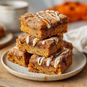 Delicious pumpkin snickerdoodle blondies cut into squares, topped with a cinnamon sugar crust and served in portions.