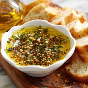 Rustic bread dipping oil with olive oil, herbs, garlic, and spices served in a small dish alongside crusty bread.