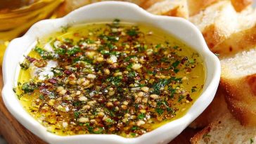 Rustic bread dipping oil with olive oil, herbs, garlic, and spices served in a small dish alongside crusty bread.