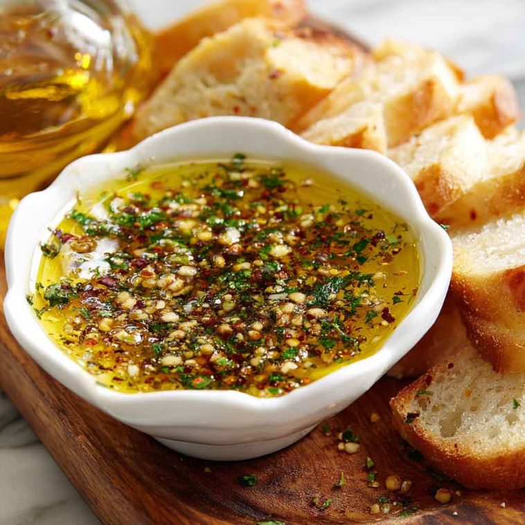 Rustic bread dipping oil with olive oil, herbs, garlic, and spices served in a small dish alongside crusty bread.