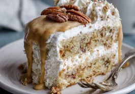 A slice of butter pecan tres leches cake soaked in creamy milk mixture, topped with whipped cream and toasted pecans.