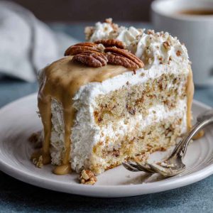 A slice of butter pecan tres leches cake soaked in creamy milk mixture, topped with whipped cream and toasted pecans.