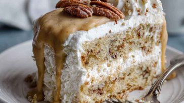 A slice of butter pecan tres leches cake soaked in creamy milk mixture, topped with whipped cream and toasted pecans.