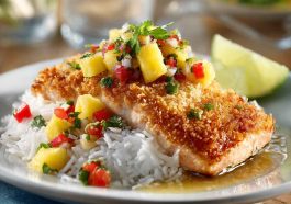 Golden coconut-crusted salmon fillets topped with bright pineapple salsa, garnished with cilantro and lime wedges.