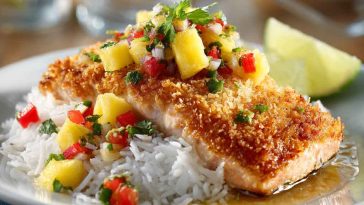 Golden coconut-crusted salmon fillets topped with bright pineapple salsa, garnished with cilantro and lime wedges.