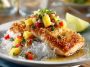 Golden coconut-crusted salmon fillets topped with bright pineapple salsa, garnished with cilantro and lime wedges.