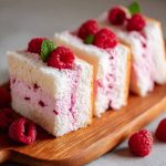 Light and fluffy raspberry angel food cake topped with fresh raspberries and a drizzle of raspberry sauce.