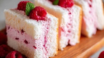 Light and fluffy raspberry angel food cake topped with fresh raspberries and a drizzle of raspberry sauce.